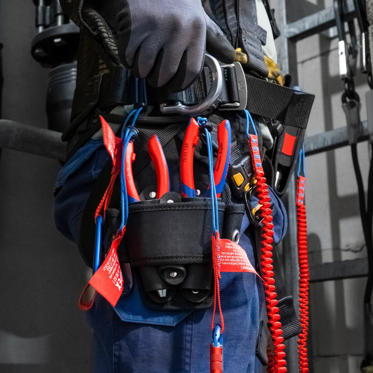 Worker equipped with safety harness carrying KNIPEX pliers secured with fall-protection tool lanyards.